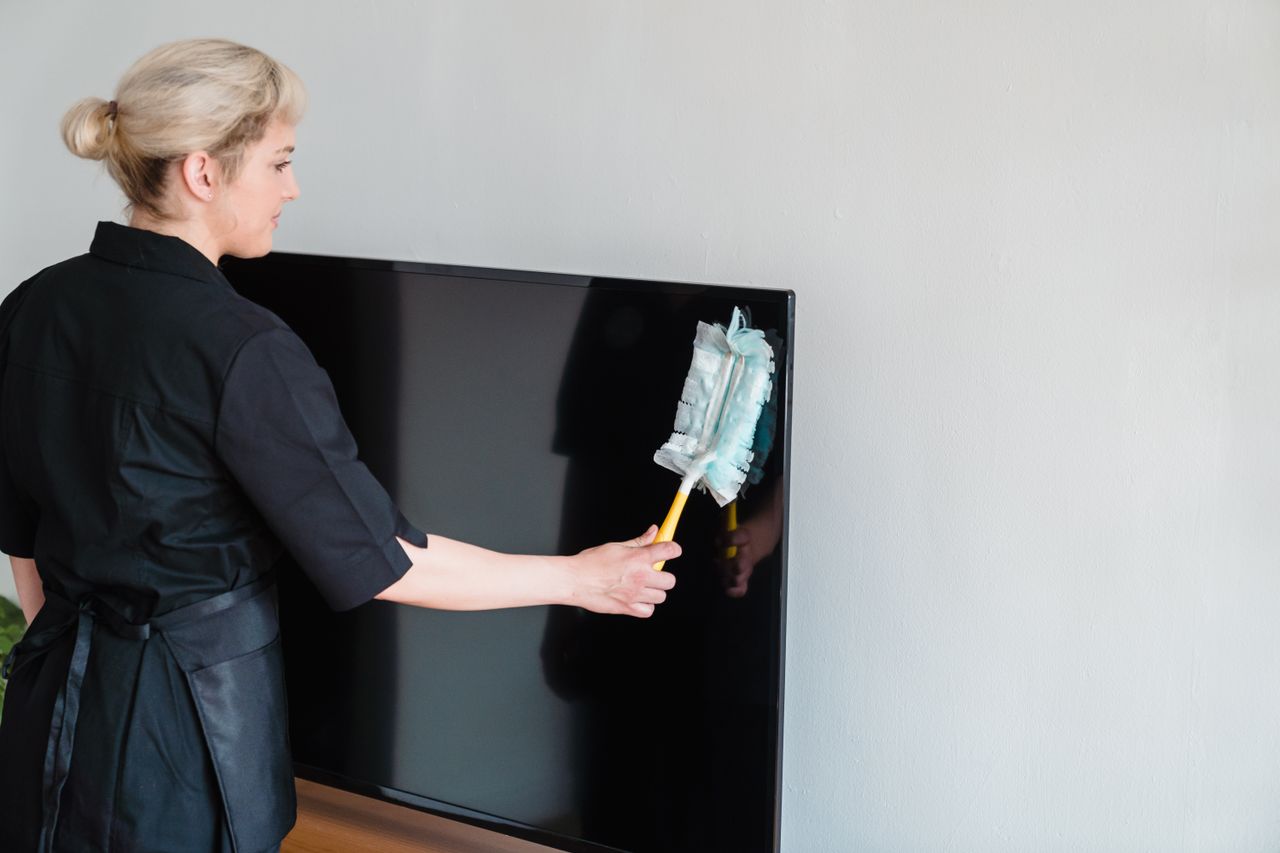 services-01 A female housekeeper performing dusting on a television screen indoors.