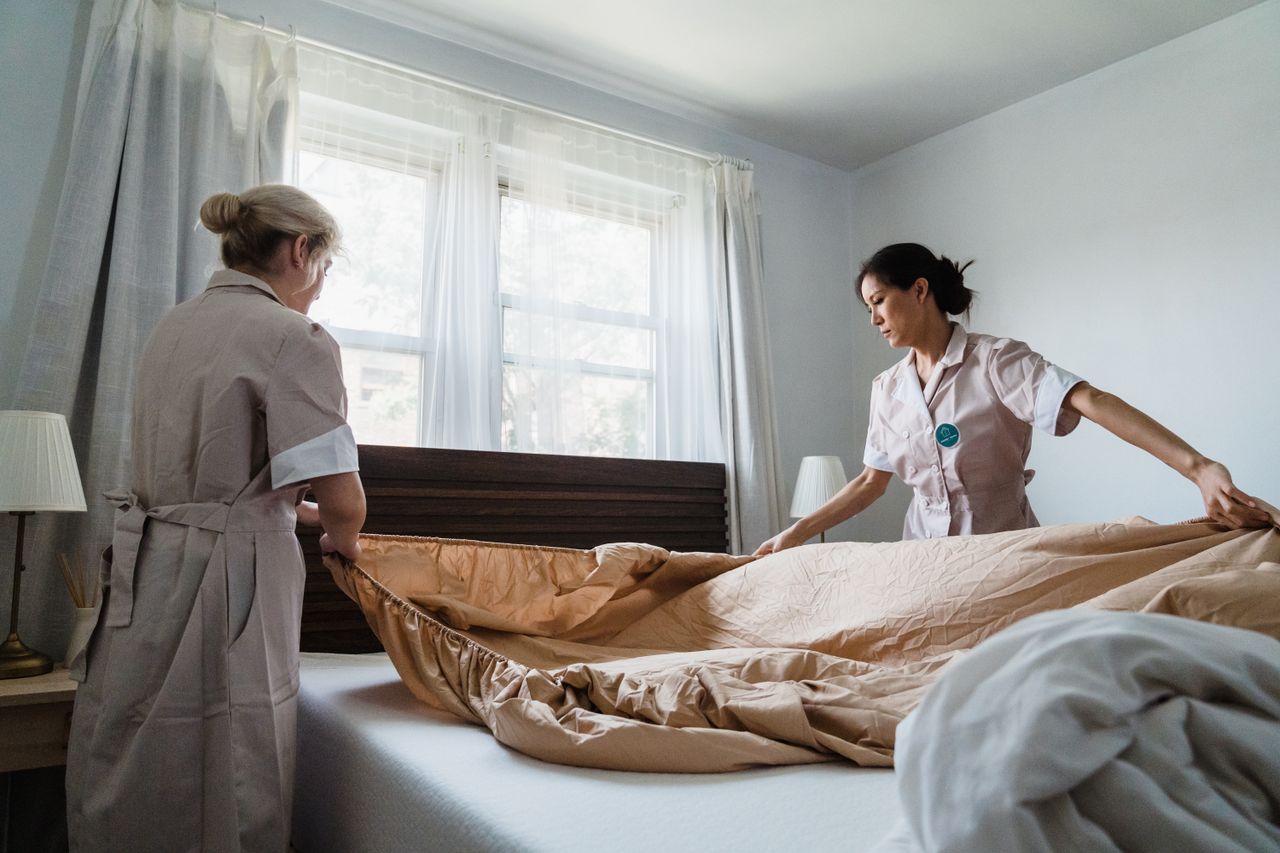 services-03 Two housekeepers professionally making a bed in a bright, comfortable room.