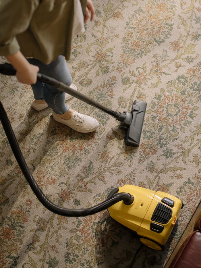 about-02 Person cleaning a floral carpet with a yellow vacuum cleaner indoors.