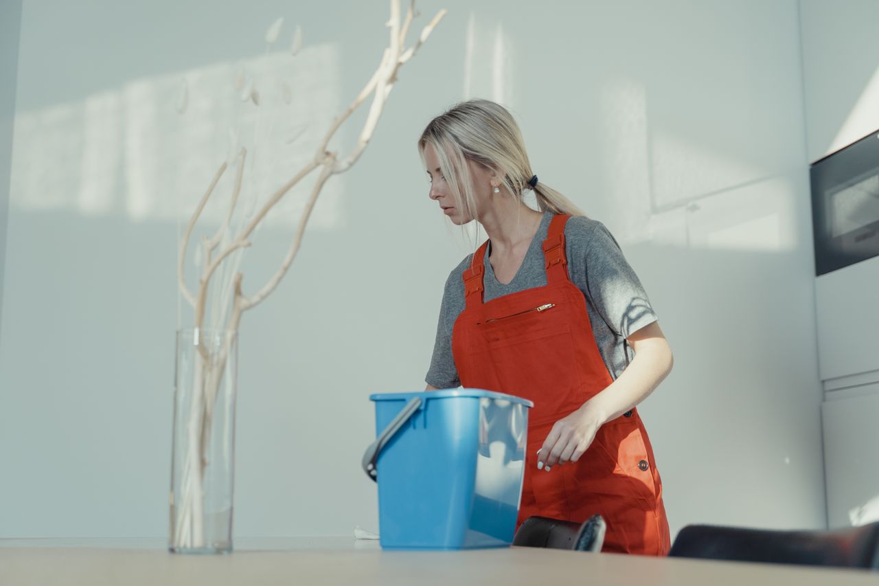 hero-img-01 A woman in a red uniform cleans indoors with a blue bucket, ensuring a spotless environment.