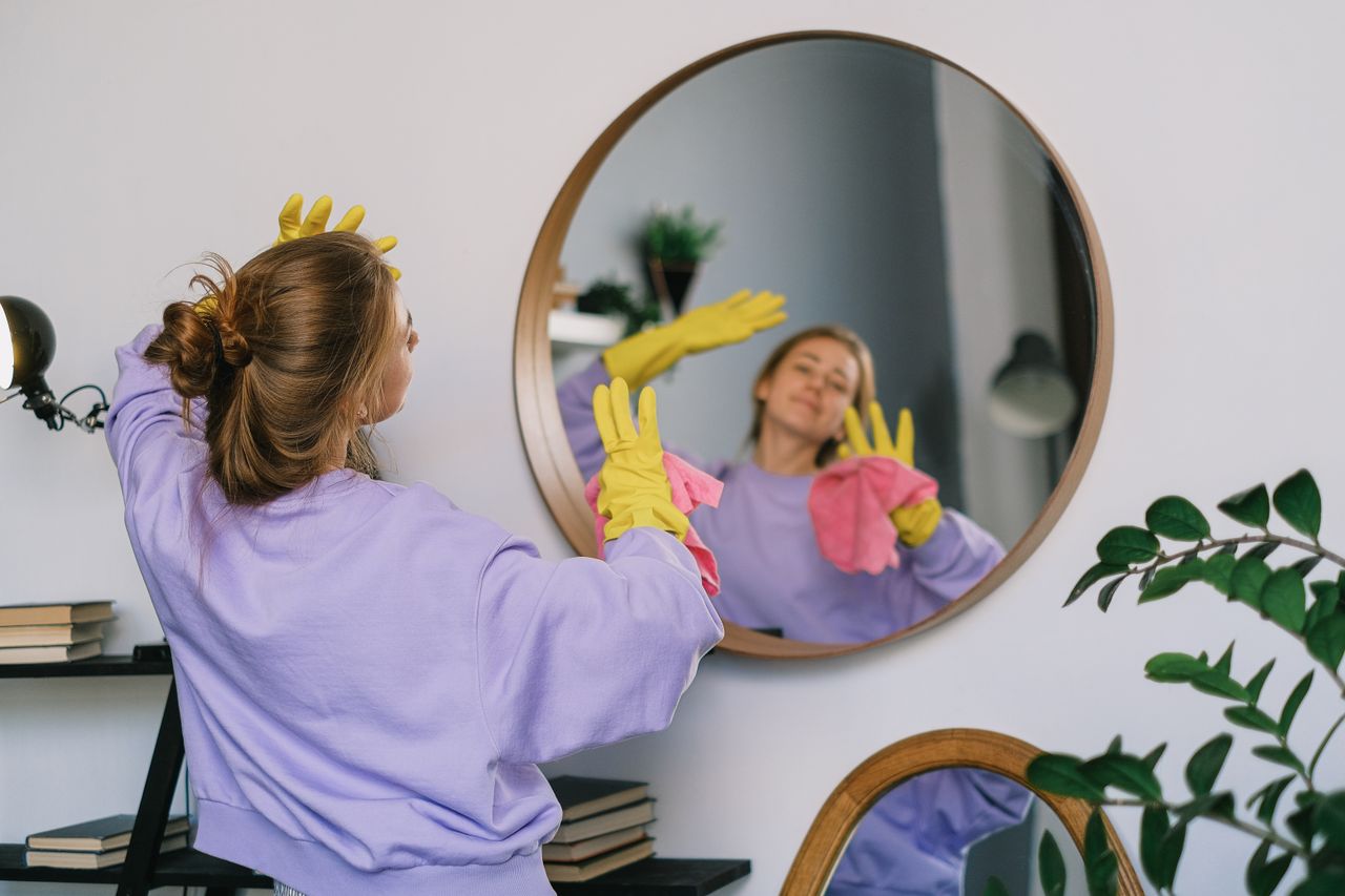 about-01 Back view of young female in casual clothes and latex gloves standing against mirror and dancing while cleaning light room in daytime